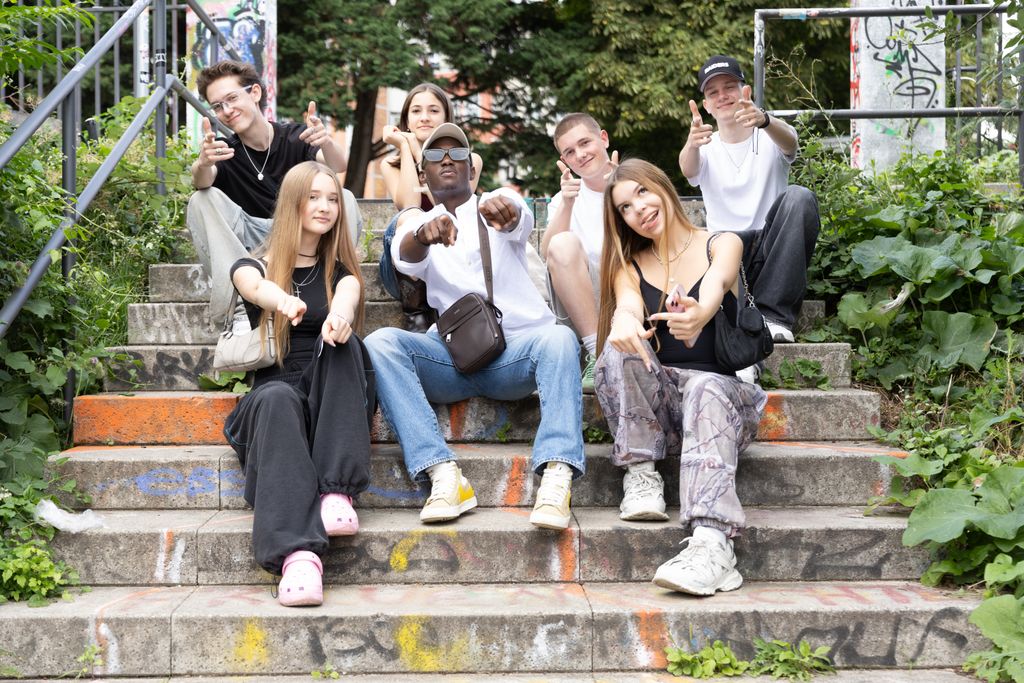A diverse group of friends sitting on urban steps with graffiti, showing playful gestures.